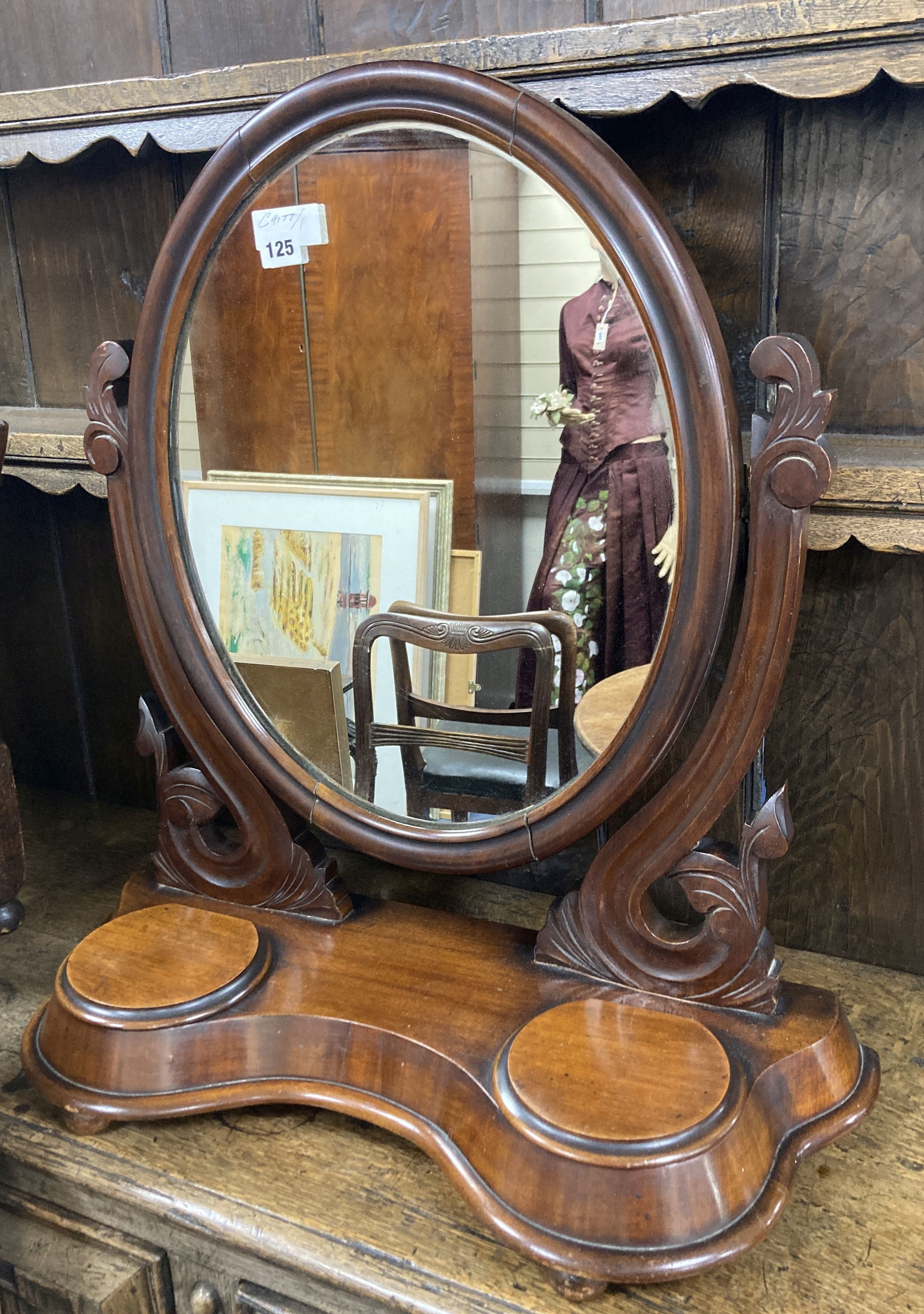 A Victorian mahogany toilet mirror of oval form above a raised platform with twin lidded compartments, width 63cm, height 71cm